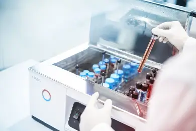 Una mano con guanti sta inserendo un campione in un bagno maria di laboratorio Lauda.