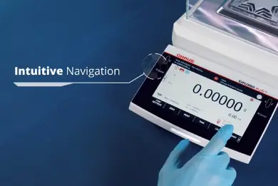 Una mano con guanto blu sta toccando lo schermo di una bilancia analitica Explorer Ohaus.