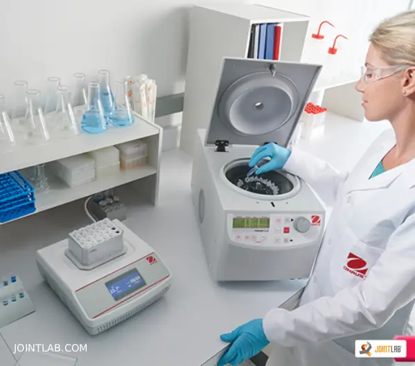 Operator inserts a test tube into the ohaus center, placed on a table next to other laboratory instruments.